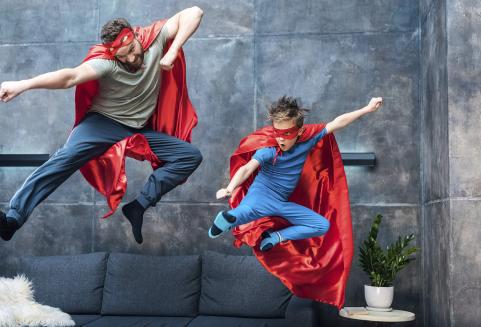 Isä ja poika hyppäävät sohvalta supermiesasut yllä.