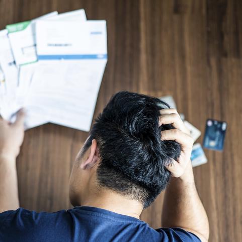 Ylhäältä kuvattu stressaantunut nuori mies pitää käsillään päätään yrittäessään selvitä luottokortti- ja lainalaskuista.