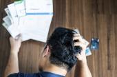 Ylhäältä kuvattu stressaantunut nuori mies pitää käsillään päätään yrittäessään selvitä luottokortti- ja lainalaskuista.