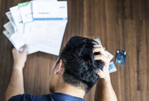 Ylhäältä kuvattu stressaantunut nuori mies pitää käsillään päätään yrittäessään selvitä luottokortti- ja lainalaskuista.