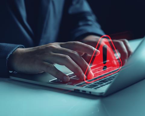 Kädet läppärin näppiksellä punainen varoituskolmio, jonka keskellä huutomerkki.