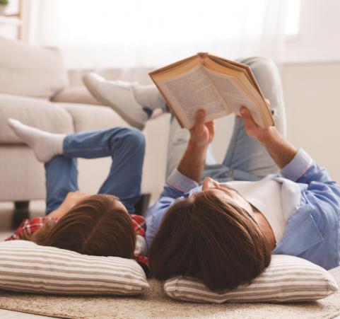 Mies ja lapsi makaavat lattialla ja lukevat kirjaa
