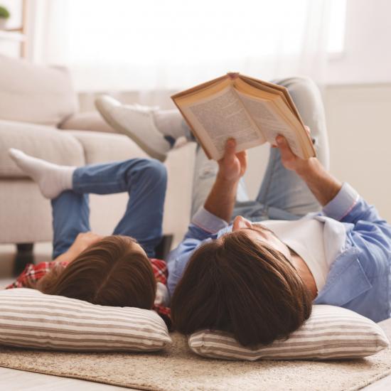 Mies ja lapsi makaavat lattialla ja lukevat kirjaa